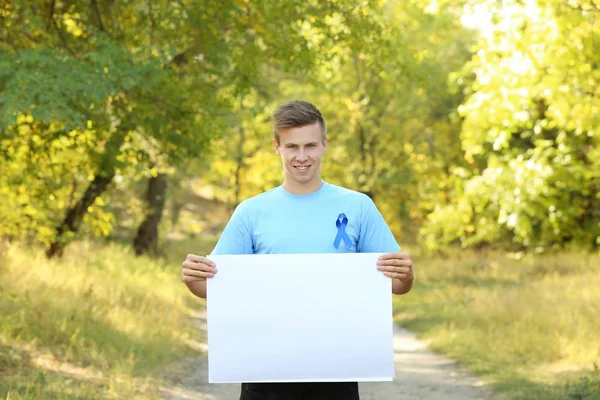 Mladý muž v tričku s modrou stužkou drží prázdný nápis venku. Koncept povědomí o rakovině prostaty — Stock fotografie