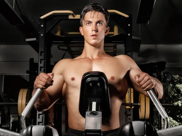 Hombre joven entrenando en una máquina de ejercicios en gimnasio —  Fotos de Stock