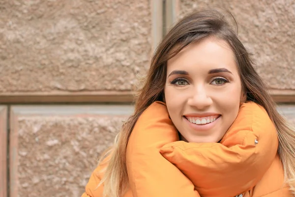 Mulher sorridente atraente em casaco de puffer laranja contra parede de tijolo — Fotografia de Stock