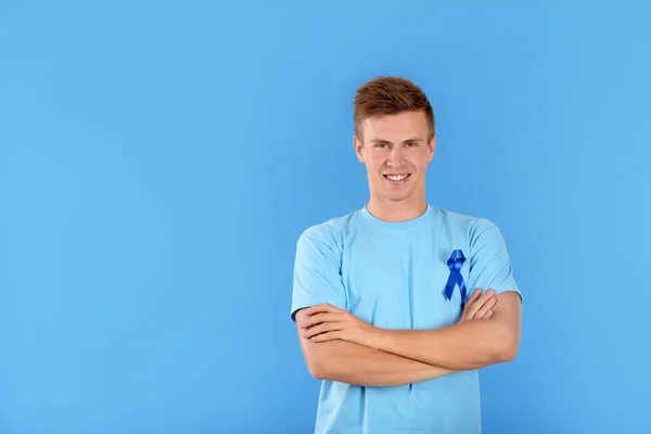 Giovane uomo che indossa t-shirt con nastro blu su sfondo colore. Concetto di sensibilizzazione sul cancro alla prostata — Foto Stock