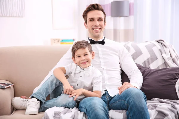 Far och son i skjortor med flugor som sitter på soffan hemma — Stockfoto