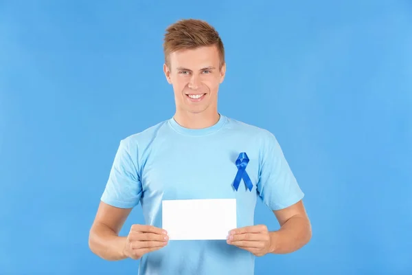 Mladý muž v tričku s modrou stužkou drží prázdnou kartu na barvu pozadí. Koncept povědomí o rakovině prostaty — Stock fotografie