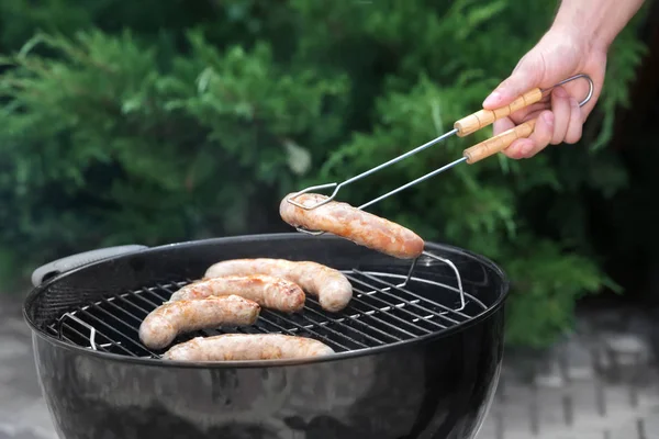 Muž připravuje lahodné klobásy na grilu venku — Stock fotografie