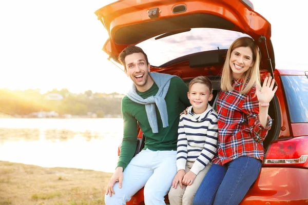 Familia joven con lindo niño sentado en el maletero del coche cerca del río —  Fotos de Stock