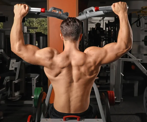 Hombre joven entrenando en una máquina de ejercicios en gimnasio — Foto de Stock