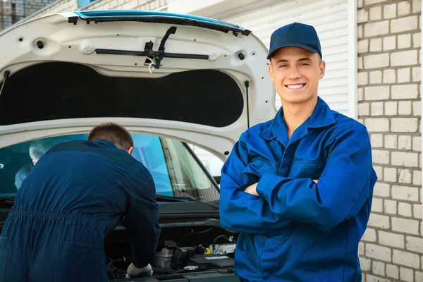 自動車整備士と彼の同僚は、屋外で車の修理 — ストック写真