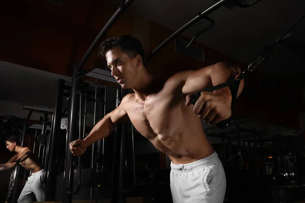 Hombre joven entrenando en una máquina de ejercicios en gimnasio — Foto de Stock