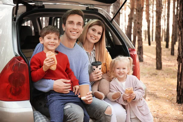 Casal jovem com seus filhos pequenos almoçando enquanto sentados no porta-malas do carro — Fotografia de Stock