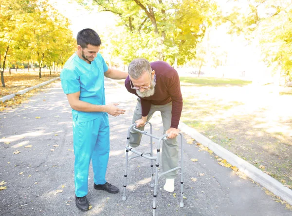 Młody opiekun spaceru z starszy mężczyzna w parku — Zdjęcie stockowe