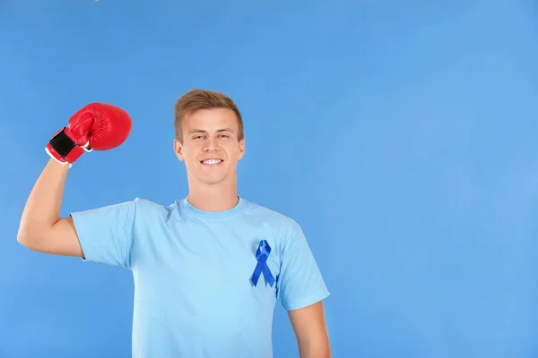 Jeune homme en t-shirt avec ruban bleu portant des gants de boxe sur fond de couleur. Concept de sensibilisation au cancer de la prostate — Photo