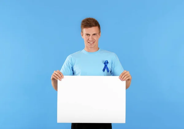Jovem em t-shirt com fita azul segurando banner em branco no fundo da cor. Conceito de consciência do câncer de próstata — Fotografia de Stock