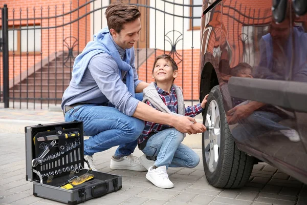 Father and son changing car wheel outdoors