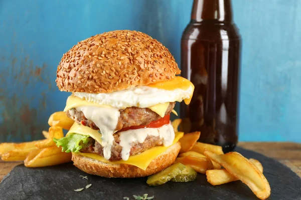 Gustoso doppio hamburger con uovo fritto sul tavolo contro la parete blu — Foto Stock