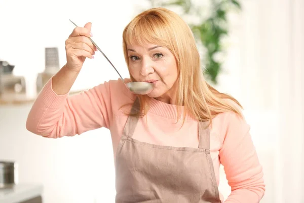 美丽成熟的妇女品尝菜在厨房做饭 — 图库照片