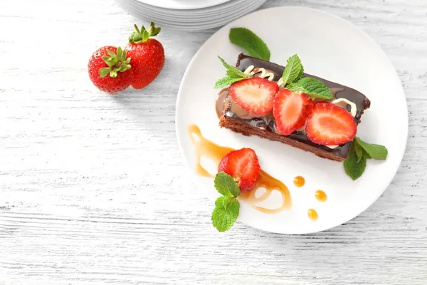 Plate with yummy chocolate cake and caramel topping on wooden table — Stock Photo, Image