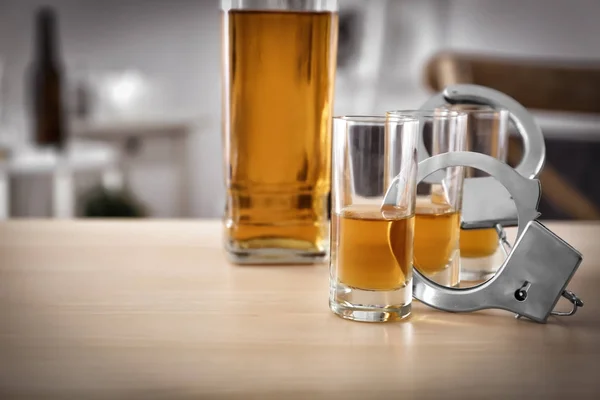 Bicchieri di alcool con manette su tavolo di legno. Concetto di dipendenza da alcol — Foto Stock