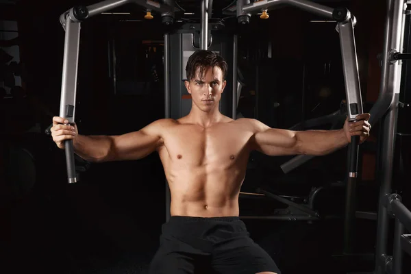 Hombre joven entrenando en una máquina de ejercicios en gimnasio —  Fotos de Stock