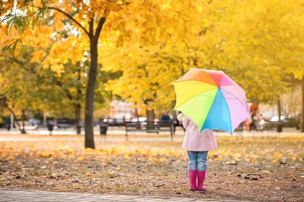Malá holčička s deštníkem rainbow v podzimním parku — Stock fotografie