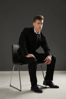 Yakışıklı adam gri duvara sandalye üzerinde oturan resmi elbiseli