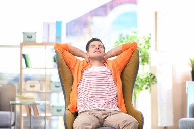 Evdeki rahat koltukta oturan yakışıklı genç adam.