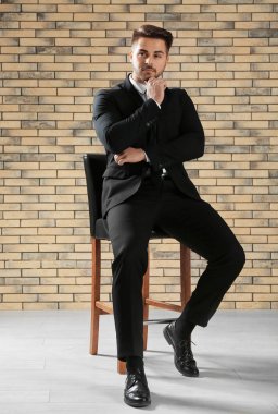 Duvara karşı sandalyeye oturmuş resmi kıyafetli yakışıklı adam