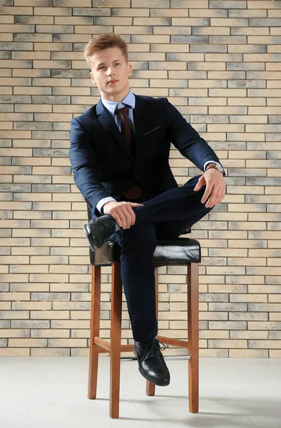 Hombre guapo en traje formal sentado en la silla contra la pared de ladrillo —  Fotos de Stock