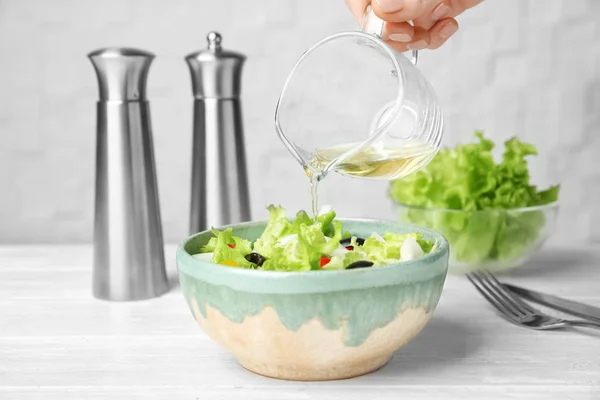 Mujer añadiendo sabroso vinagre de manzana en ensalada con verduras en la mesa —  Fotos de Stock