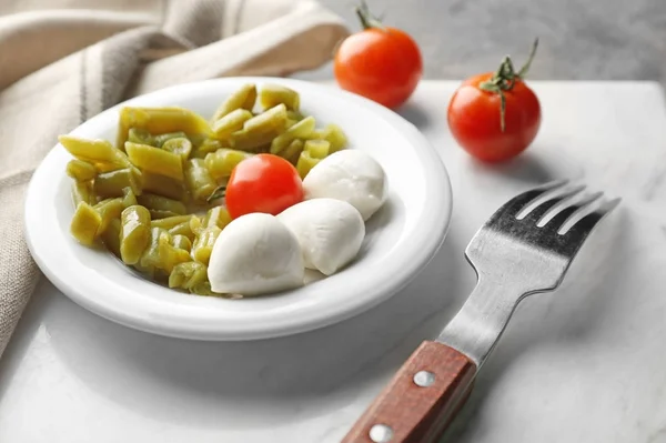 Plate with canned green beans, tomatoes and mozzarella on table