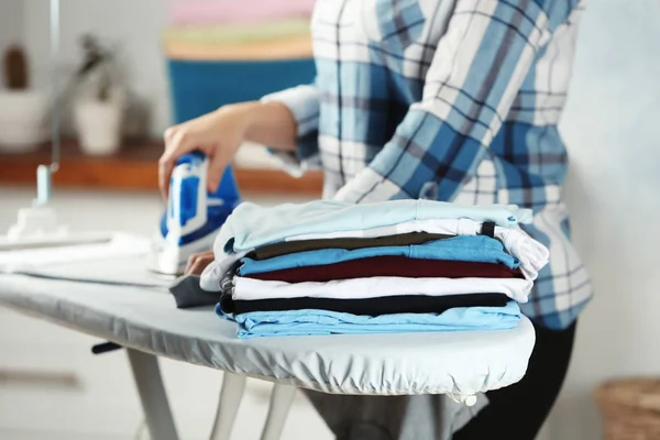 Stack of laundry and woman ironing clothes indoors — Stock Photo, Image