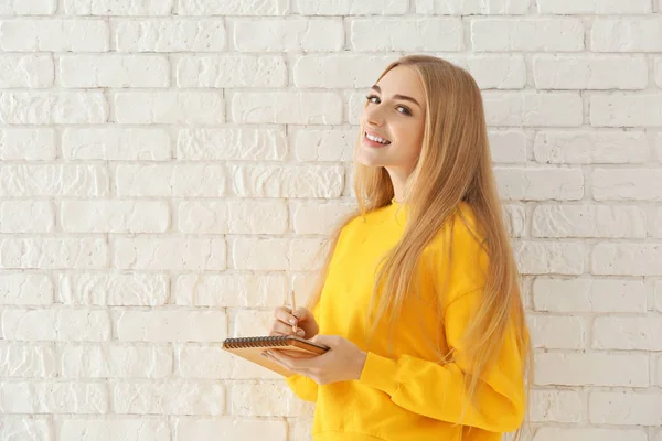 Smiling woman in yellow sweatshirt on brick wall background