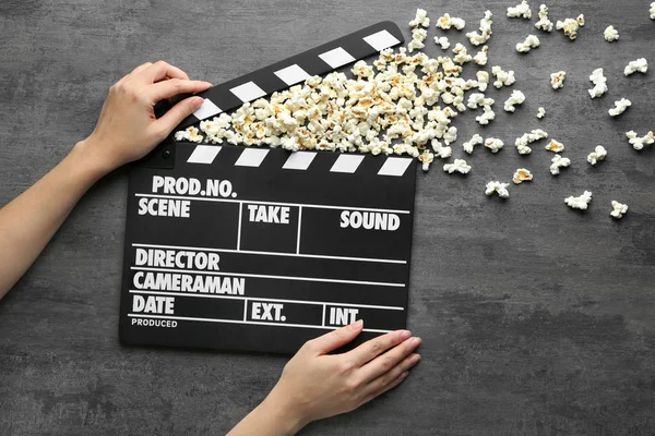Kvinna som håller filmen kläpp med popcorn skytte ur det på grå bakgrund — Stockfoto