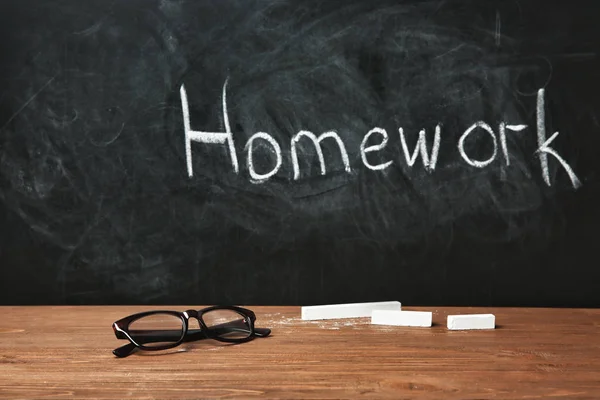 メガネと単語 宿題と黒板の近くのテーブルにチョークの部分 — ストック写真