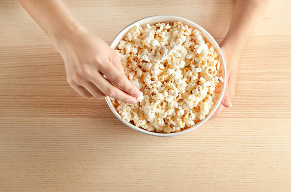 Женщина ест вкусный попкорн за столом, вид сверху
