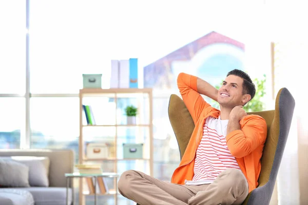 Beau jeune homme assis dans un fauteuil confortable à la maison — Photo