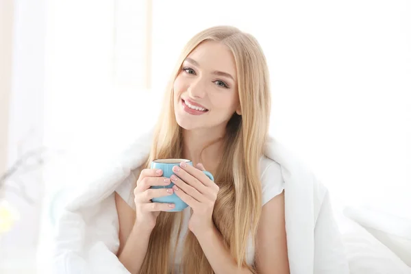 Jonge mooie lachende vrouw met kopje koffie in bed thuis — Stockfoto