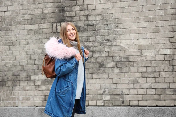 迷人的时髦女孩在温暖的夹克与背包附近砖墙壁室外 — 图库照片
