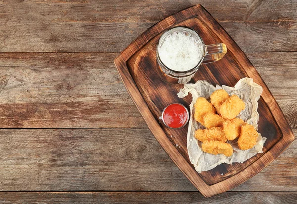 Holzbrett mit leckeren Chicken Nuggets, Bier und Soße auf dem Tisch — Stockfoto