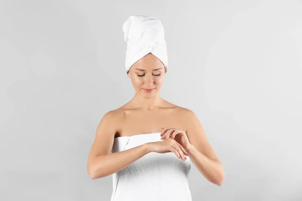 Mujer joven aplicando crema corporal sobre fondo claro — Foto de Stock