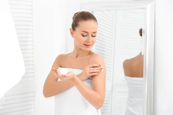 Mujer joven aplicando crema corporal en el baño — Foto de Stock