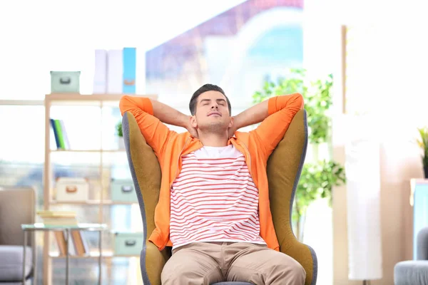 Guapo joven sentado en cómodo sillón en casa — Foto de Stock