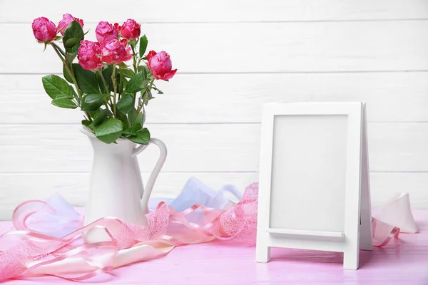 Jarra con rosas y marco vacío en la mesa — Foto de Stock