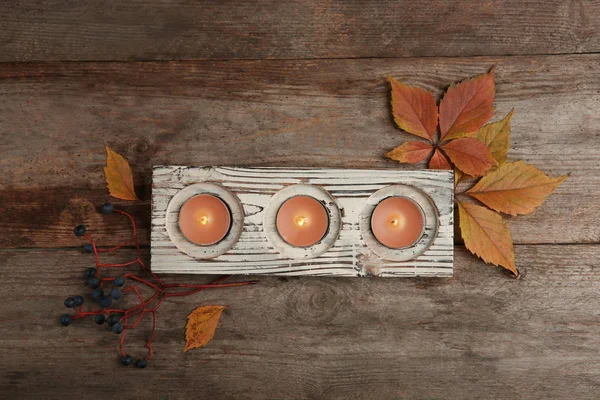 Composition with burning candles and autumnal leaves on wooden background, top view — Stock Photo, Image