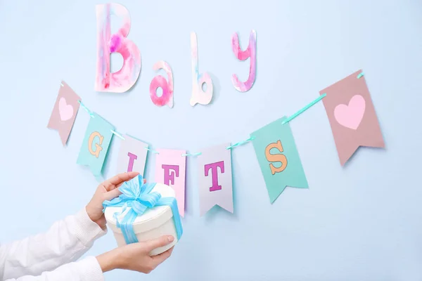 Mulher segurando caixa de presente para festa de chá de bebê perto da parede decorada dentro de casa — Fotografia de Stock