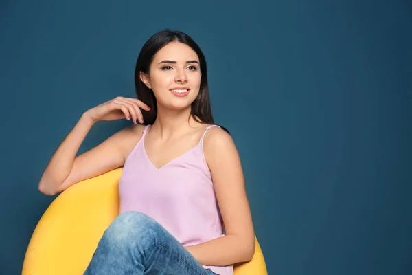 Smilende ung kvinde sidder i gul lænestol på farve baggrund - Stock-foto
