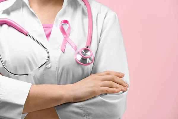 Doctor with pink ribbon on robe against color background. Breast cancer awareness concept — Stock Photo, Image
