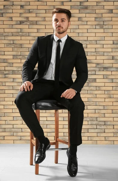 Handsome man in formal suit sitting on chair against brick wall