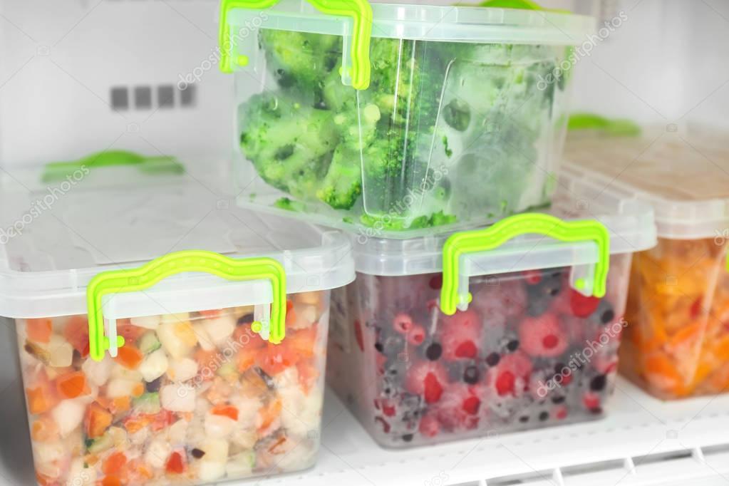 Containers with frozen berries and vegetables in freezer, closeup