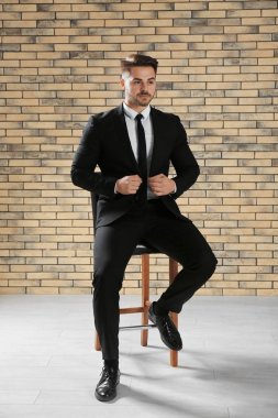 Duvara karşı sandalyeye oturmuş resmi kıyafetli yakışıklı adam