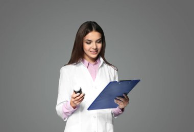 Genç kadın eczacı ile ilaç ve gri arka plan üzerinde Pano