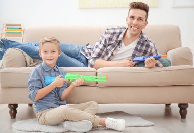 Sevimli çocuk ve babası evde oyuncak silahlarla oynayan